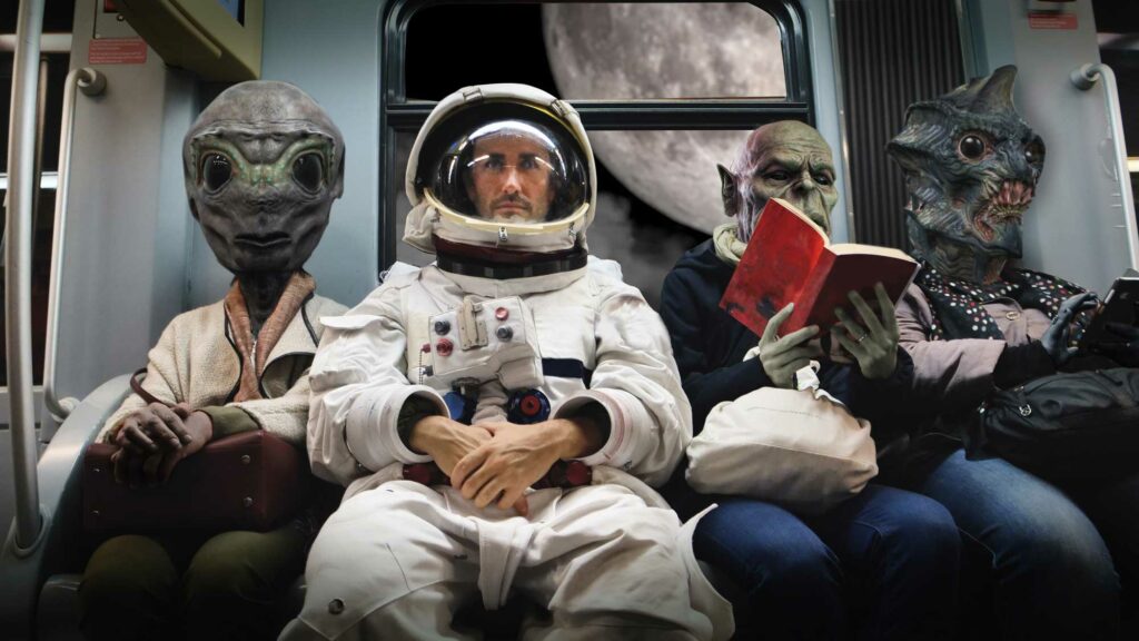 spaceman sitting between aliens on subway